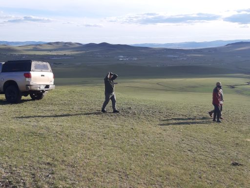 Auf der Suche nach einem Biwakplatz Zwei Personen und ein Auto auf einer weiten, offenen Graslandschaft.