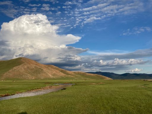 Ein blick in die Landschaft Weite Landschaft mit grünen Wiesen, einem kleinen Fluss und dramatischem Himmel.